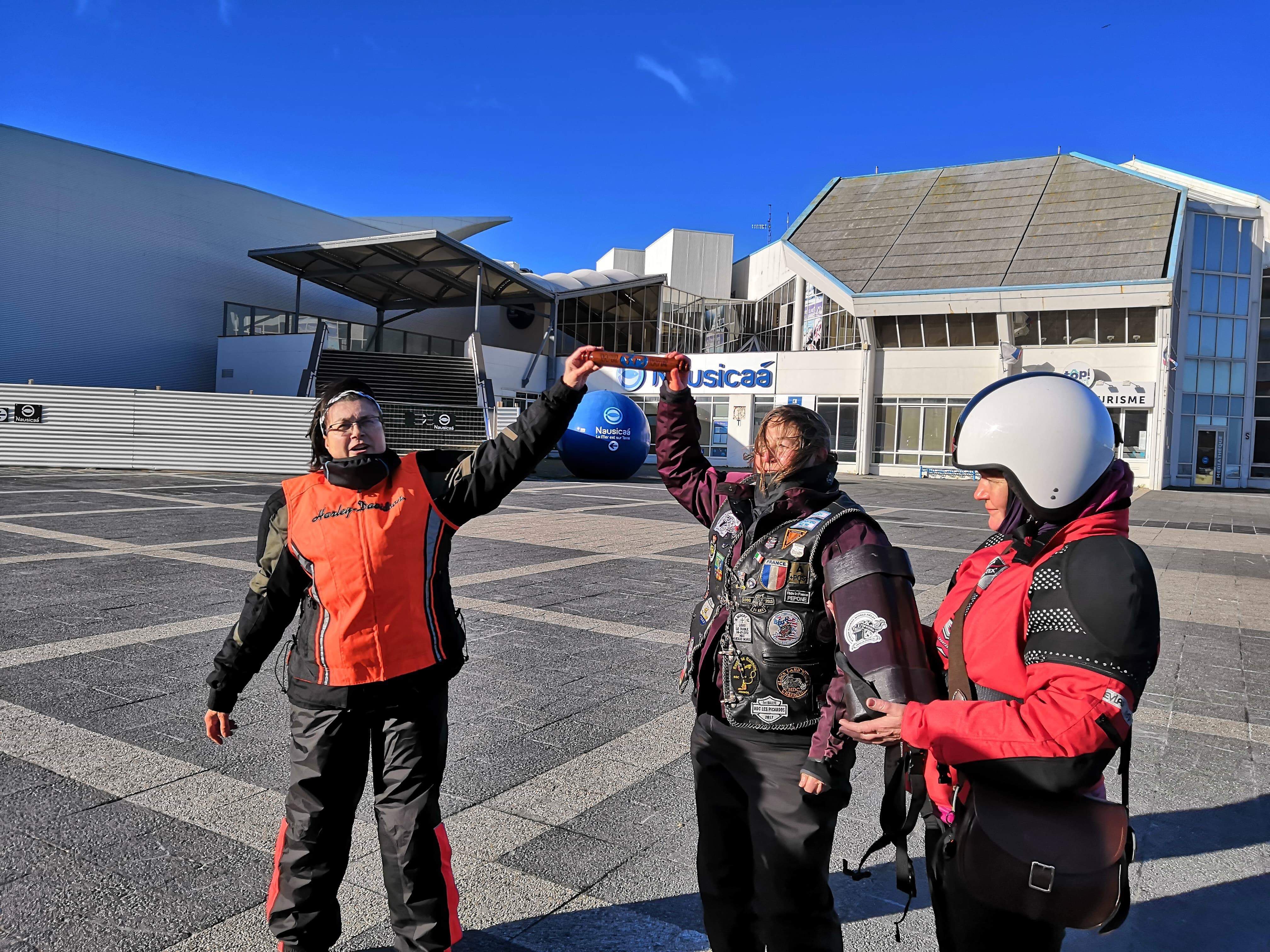 French lady motorcyclists holding up the WRWR baton which has been safely delivered by the English motorcyclists