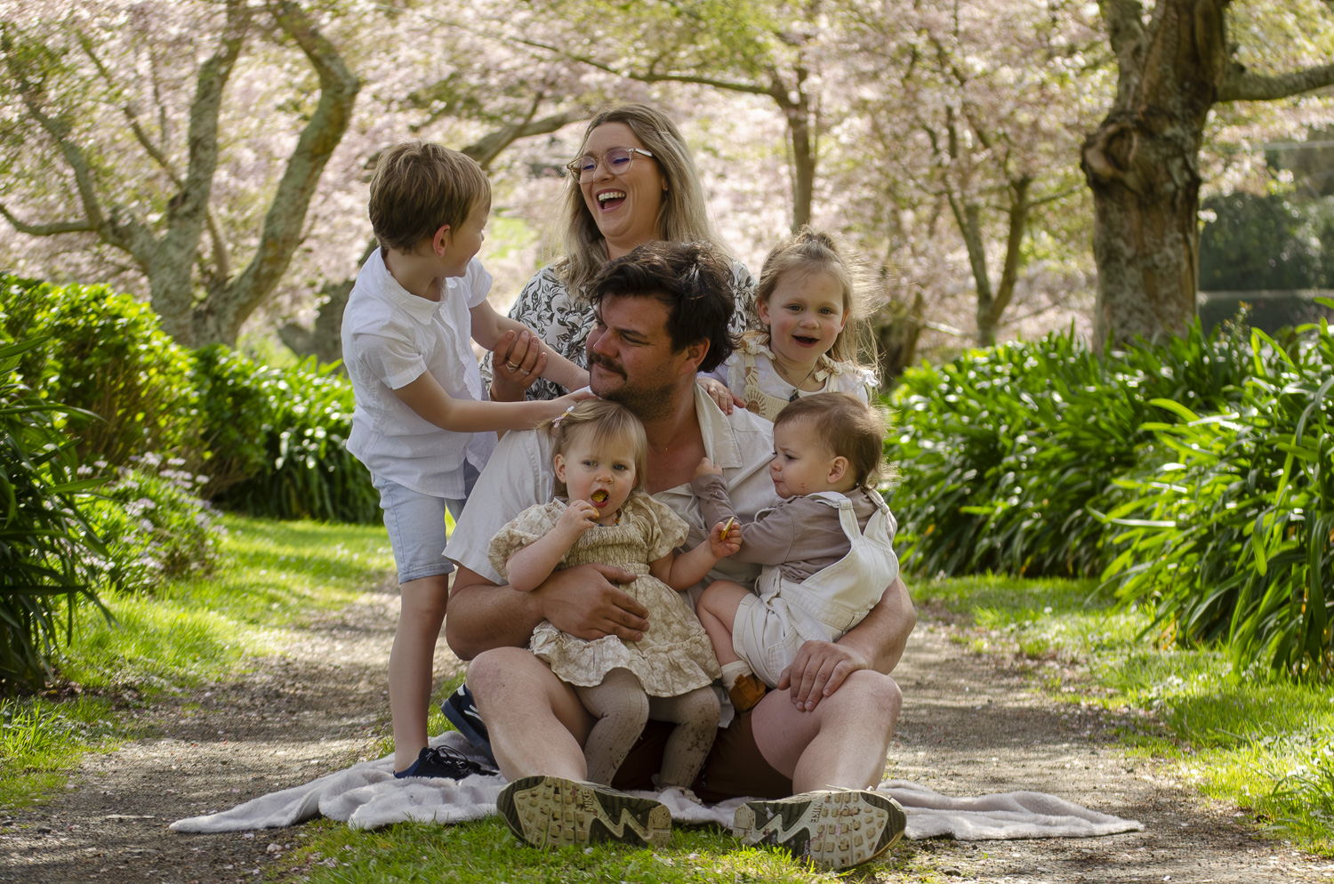 A photograph of a young family sat under cherry blossom trees. Taken by Te Awamutu, Waikato based photographer, Donna from Donna May Photography.