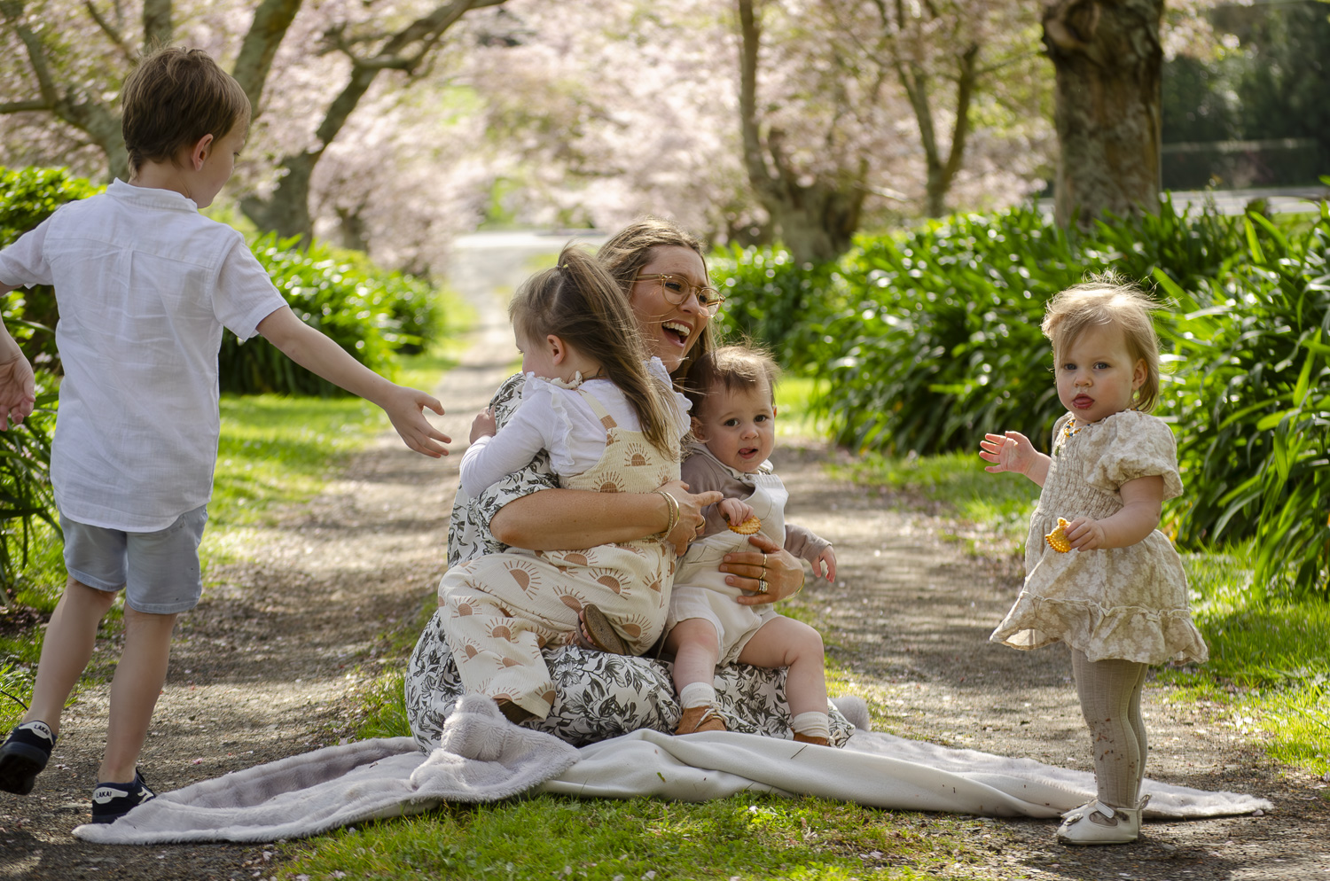 A photograph of a mum and her young family sat under cherry blossom trees. Taken by Te Awamutu, Waikato based photographer, Donna from Donna May Photography.