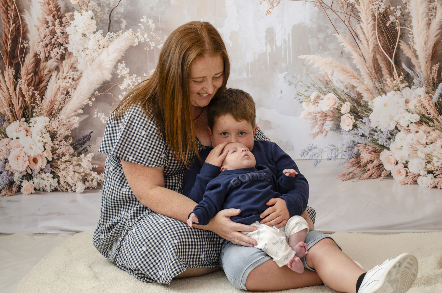A family portrait photo of a mum cradling her young son who's cradling his newborn brother. Taken by Te Awamutu, Waikato based photographer, Donna from Donna May Photographer.