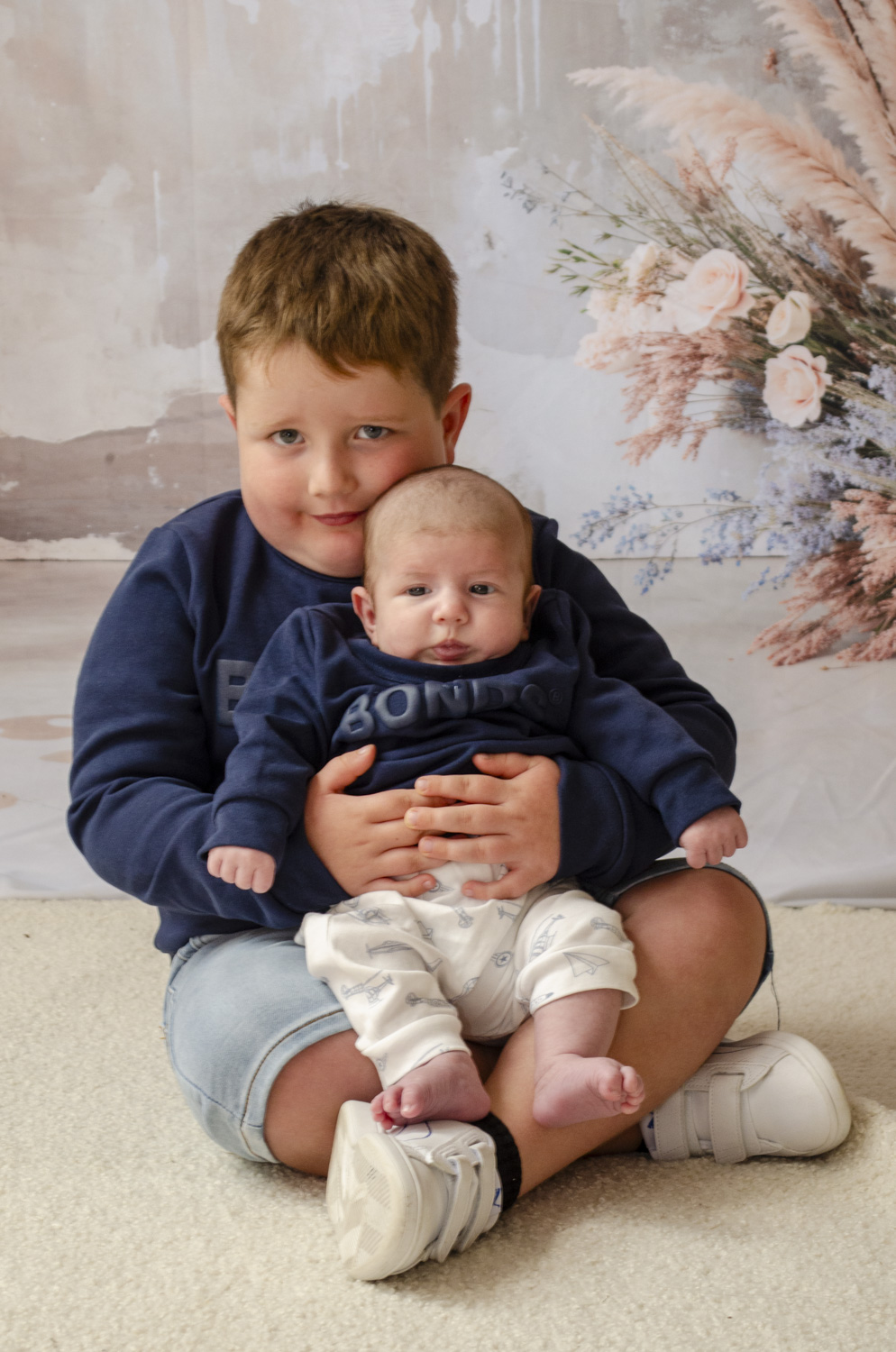 A family portrait photo of a little boy holding his newborn baby brother. Taken by Te Awamutu, Waikato based photographer, Donna from Donna May Photography.