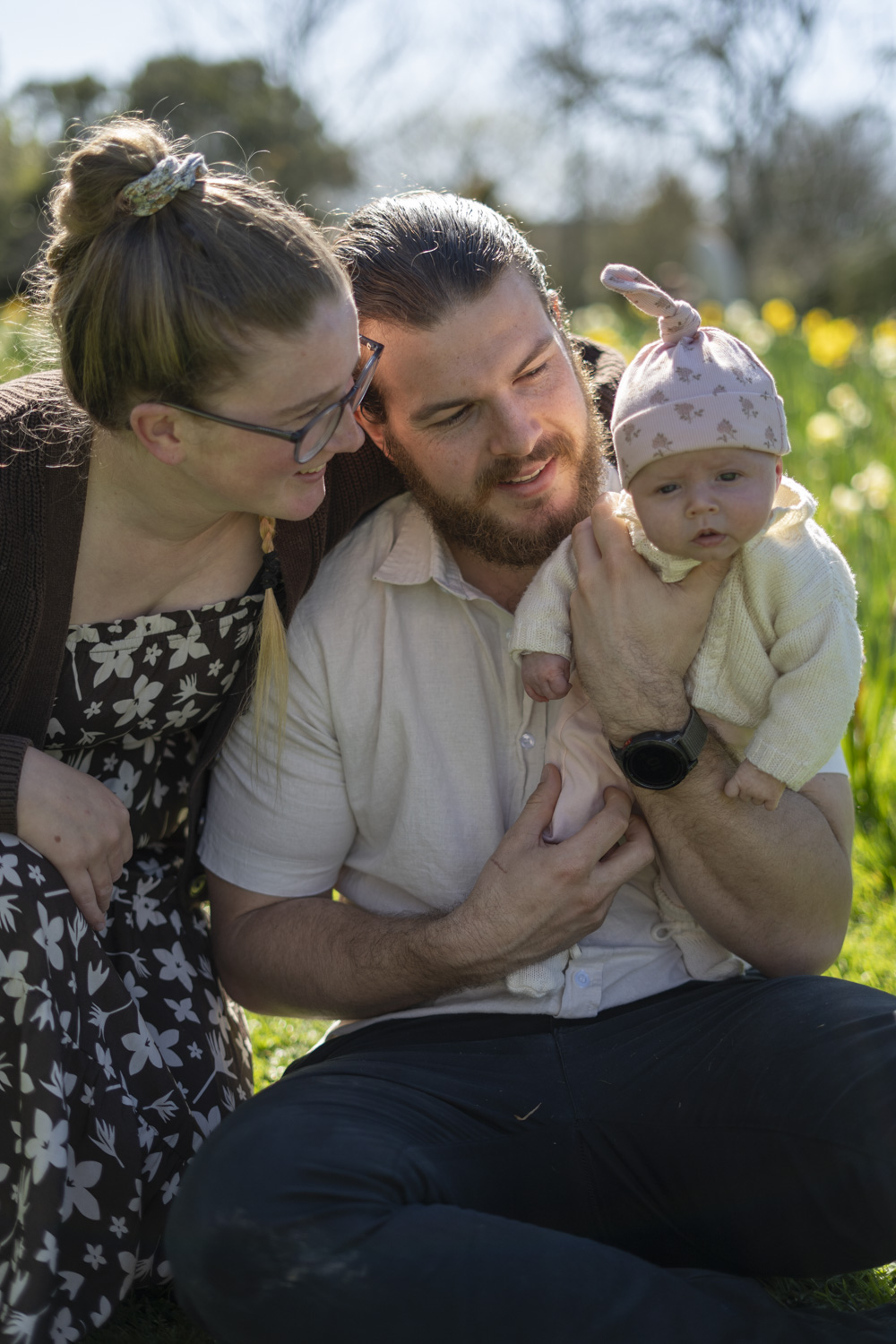 A family portrait photo of a young couple and their newborn baby amongst the daffodils. Taken by Te Awamutu, Waikato based photographer, Donna from Donna May Photography.