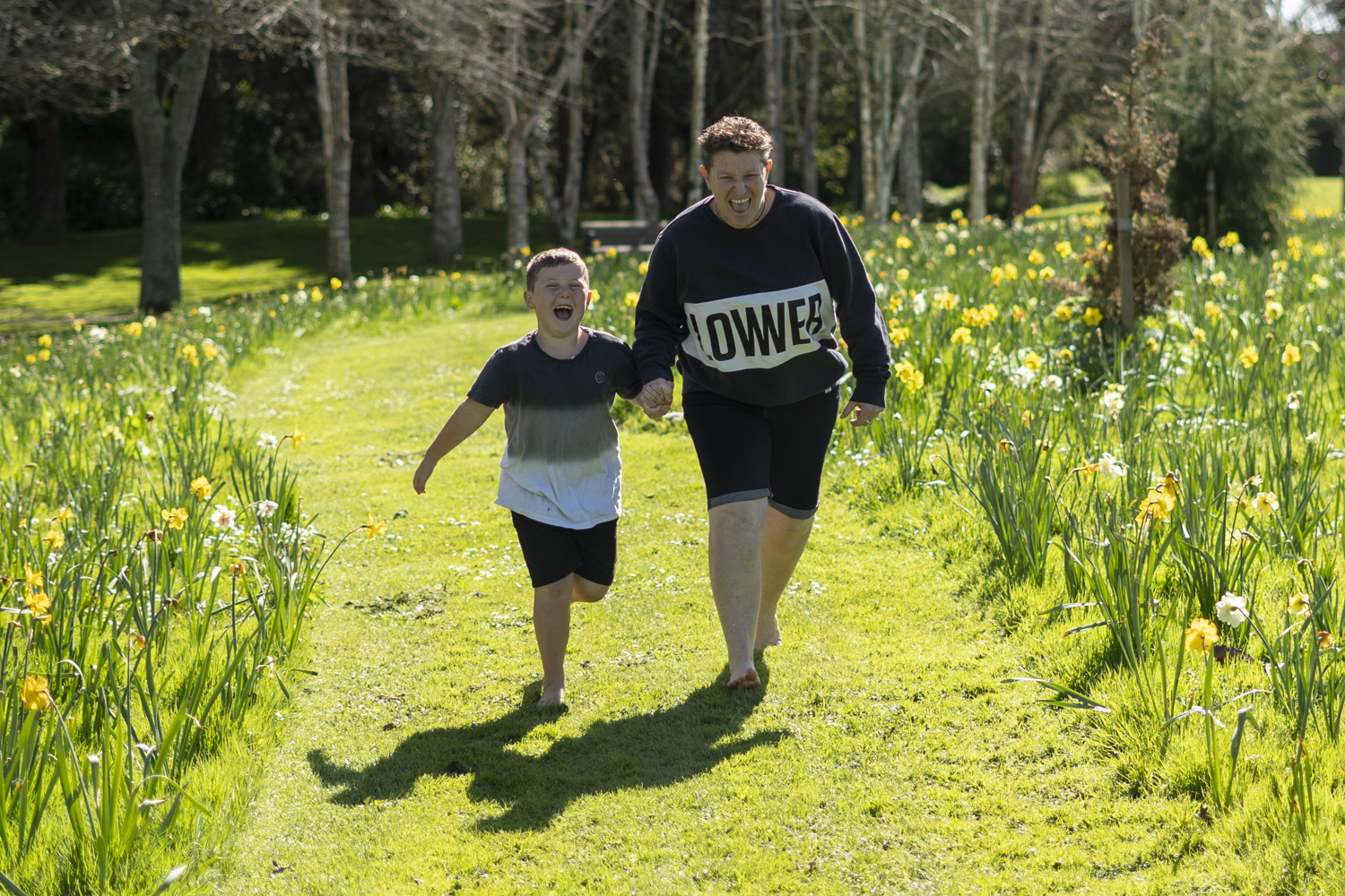 A lifestyle family portrait photo of a auntie running with her nephew amongst the daffodils. Photo taken by Te Awamutu, Waikato based photographer Donna from Donna May Photography.