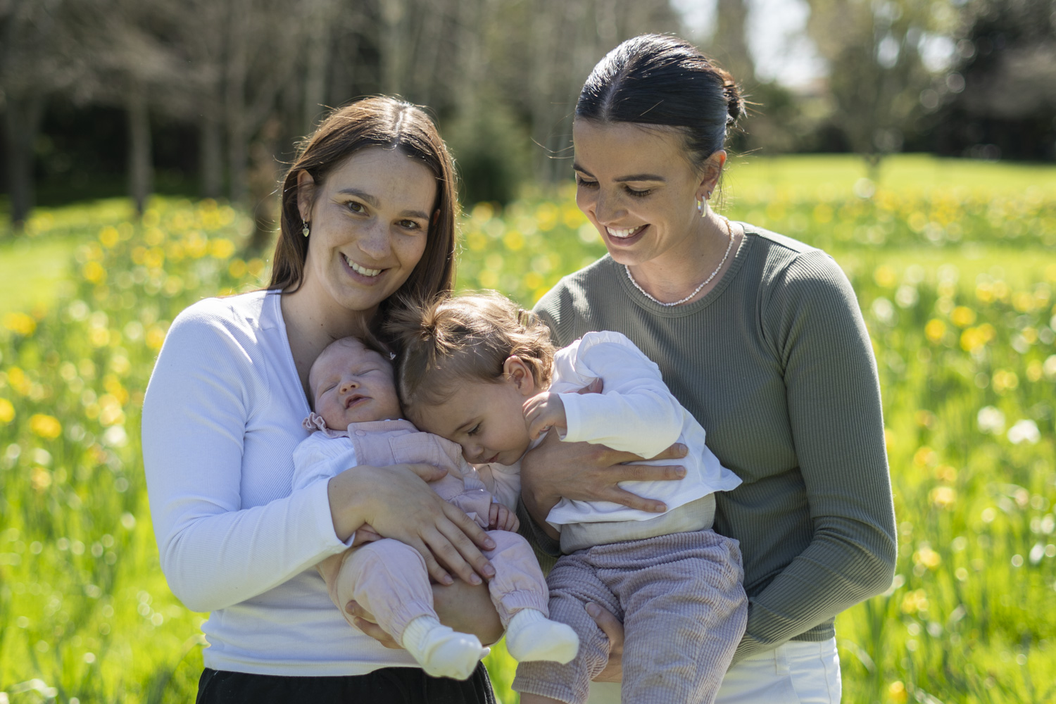 A portrait photo of two friends and their babies amongst the daffodils. Taken by Te Awamutu, Waikato based photographer, Donna from Donna May Photography.