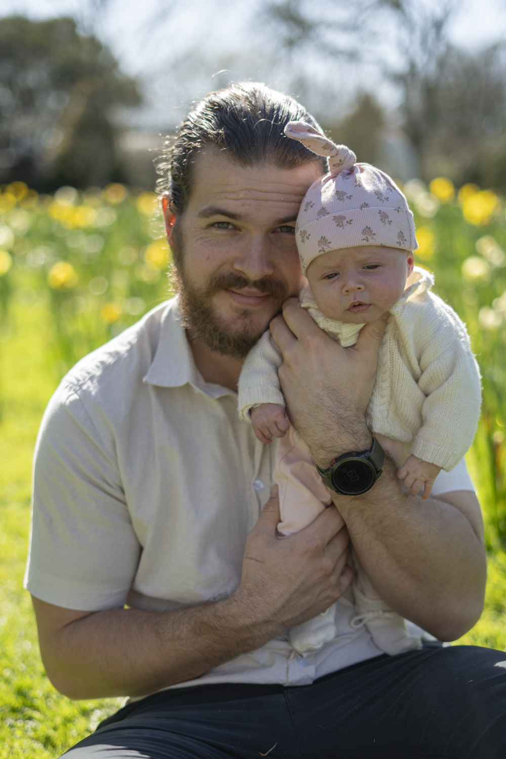 A portrait photo of a young dad holding his infant daughter amongst the daffodils. Taken by Te Awamutu, Waikato based photographer, Donna form Donna May Photography