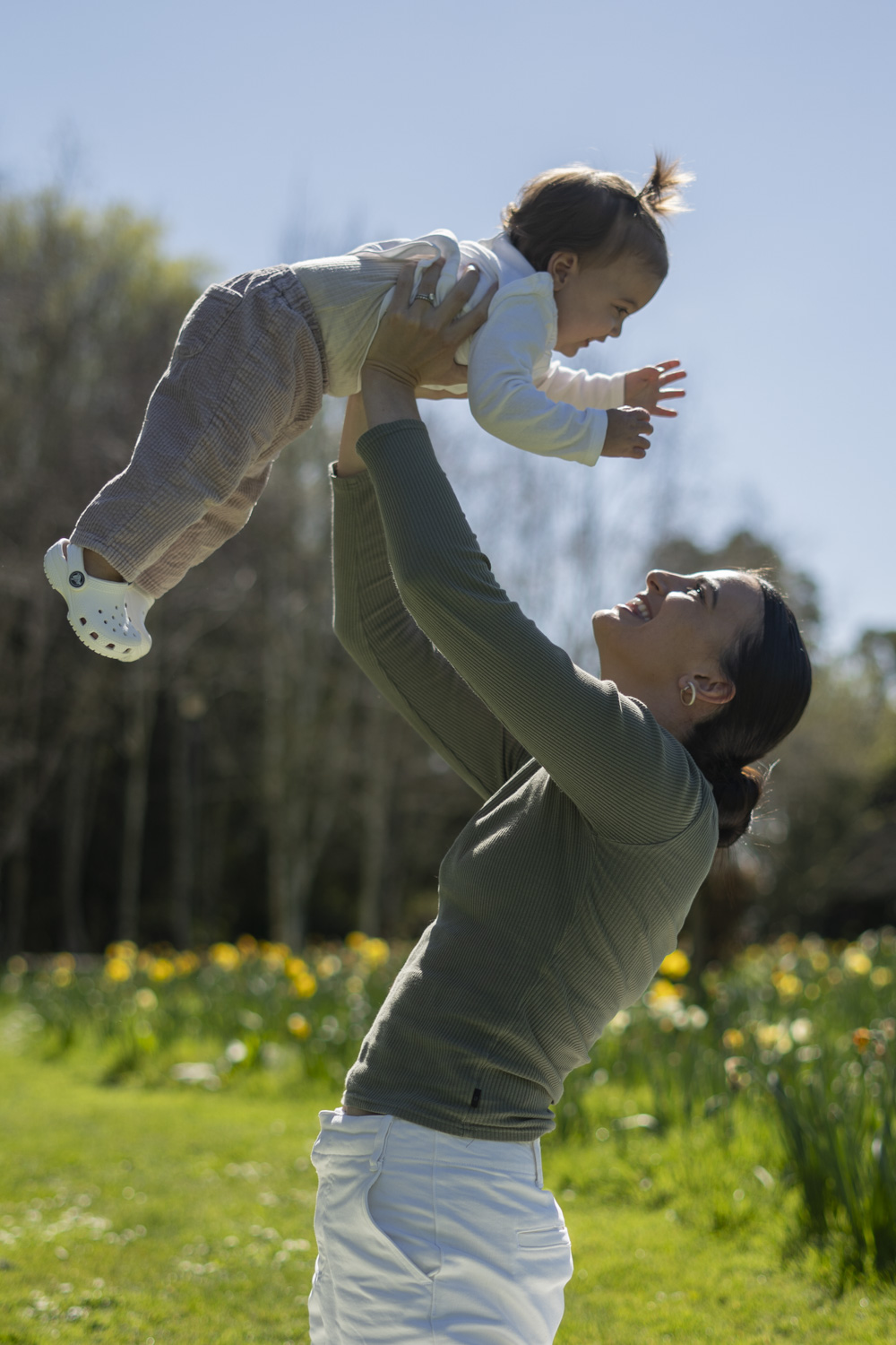 A lifestyle portrait photo of a mum lifting her young daughter in the air amongst the daffodils. Taken by Te Awamutu, Waikato based photographer, Donna form Donna May Photography