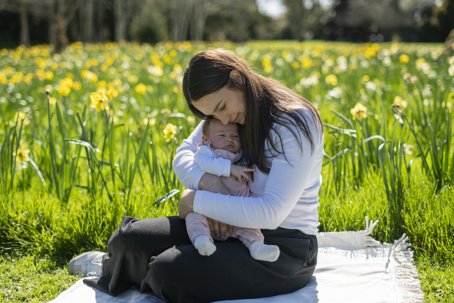 A portrait photo of a young mum holding her infant daughter amongst the daffodils. Taken by Te Awamutu, Waikato based photographer, Donna form Donna May Photography