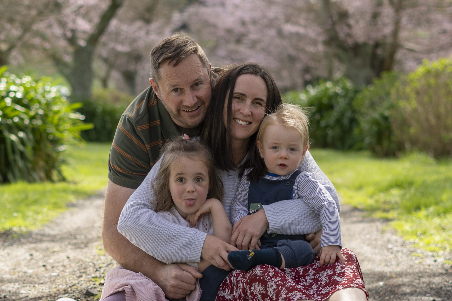 A photograph of a young family sat under cherry blossom trees. Taken by Te Awamutu, Waikato based photographer, Donna from Donna May Photography.