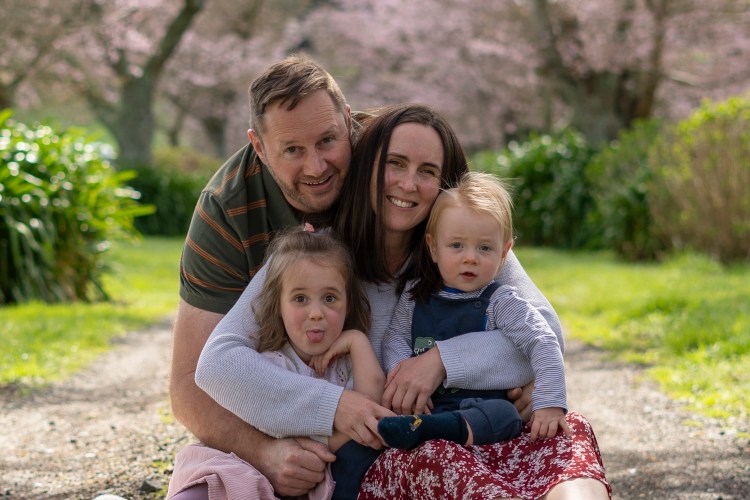 A photograph of a young family sat under cherry blossom trees. Taken by Te Awamutu, Waikato based photographer, Donna from Donna May Photography.