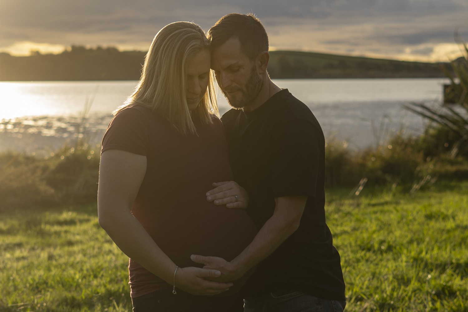A maternity photo of a couple next to a lake in Te Awamutu. Taken at golden hour by Donna from Donna May Photography. A Waikato, Te Awamutu based lifestyle family photographer.