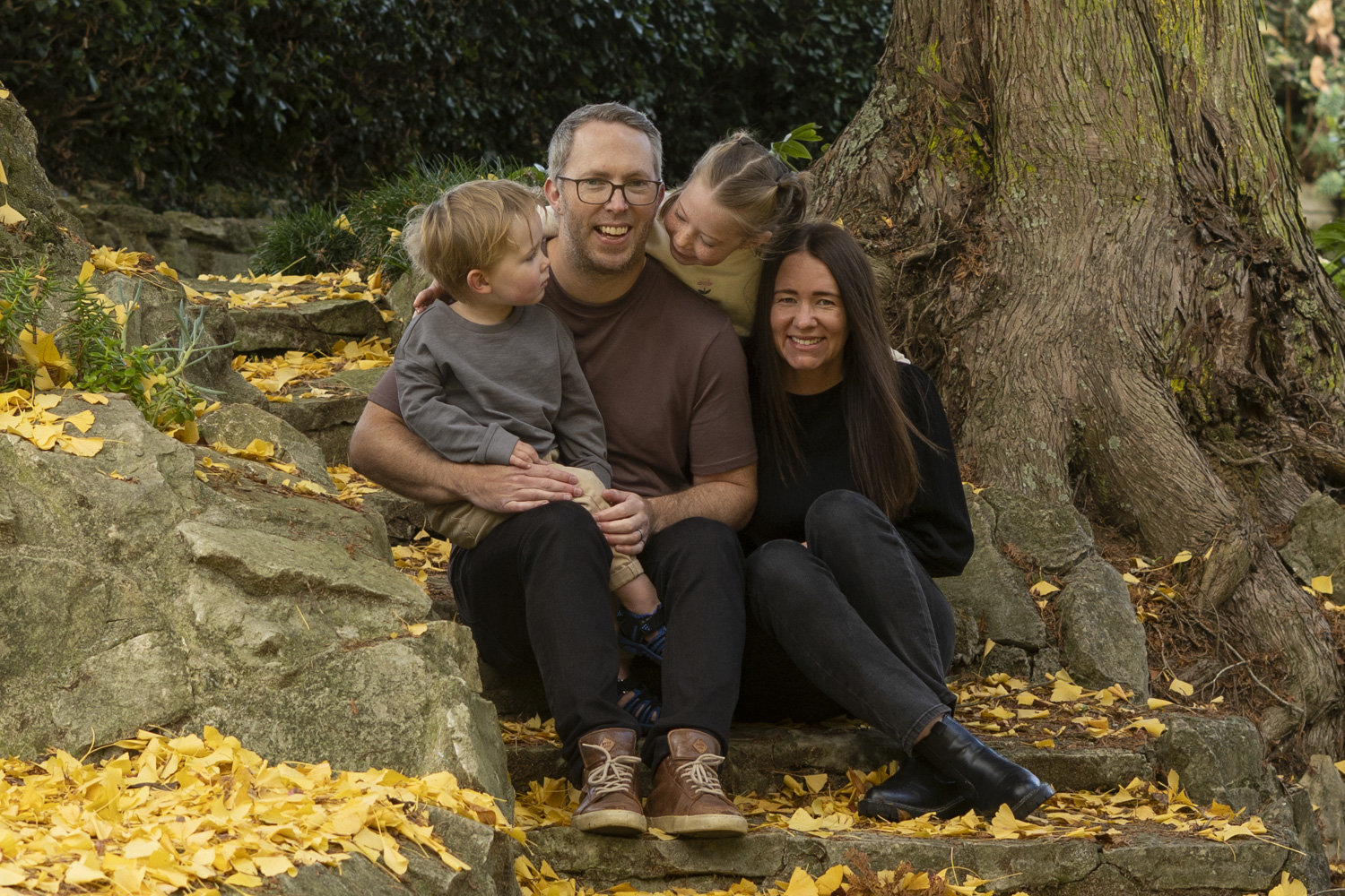 A portrait photo of a young family sat on some steps in a park in autumn. Taken by Te Awamutu, Waikato based photographer, Donna from Donna May Photography